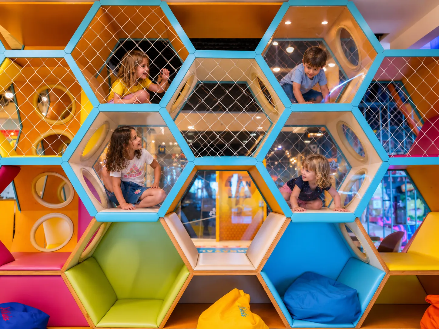 Patru copii jucându-se împreună în structura cu celule hexagonale colorate din zona de joacă KLANkids Carnaval
