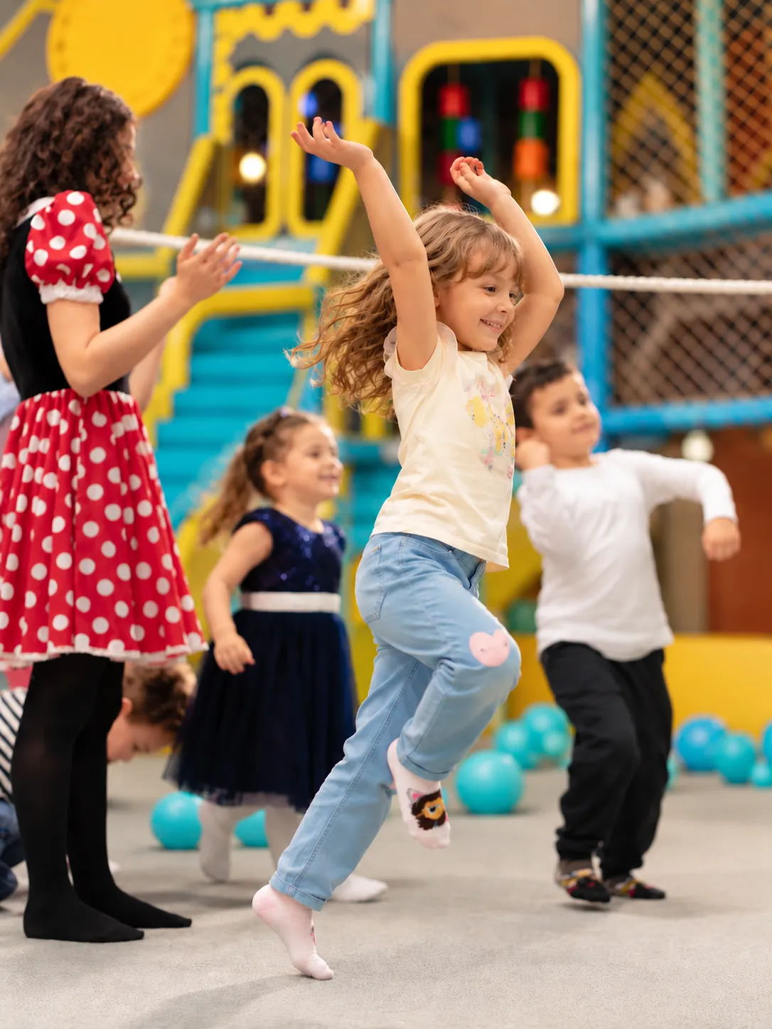 Fetiță dansând veselă cu mâinile sus, alături de alți copii și o animatoare, în zona de joacă KLANkids Carnaval