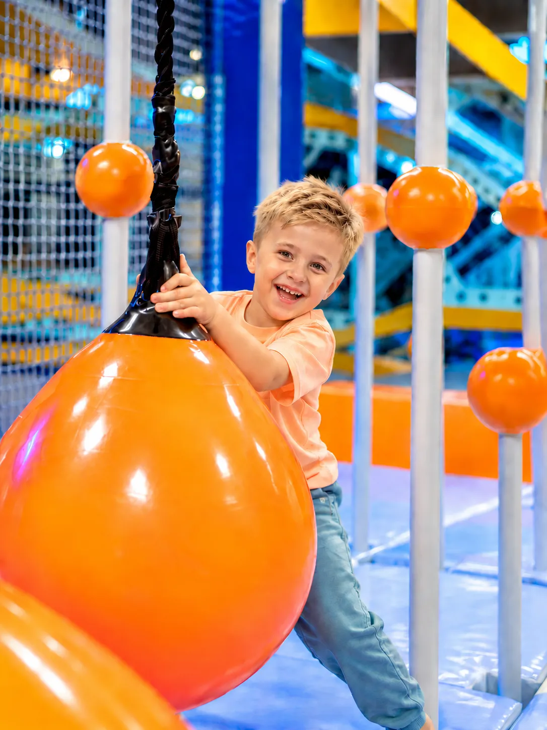 Băiat care râde agățat de un balon portocaliu pe traseul de aventură KLANkids